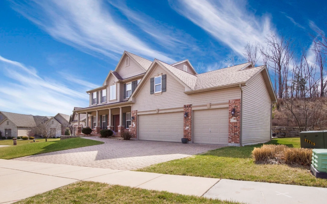 Two-story beige house with multiple windows, a front yard, and a three-car garage, set against a clear blue sky with wispy clouds—perfect for any painting portfolio.